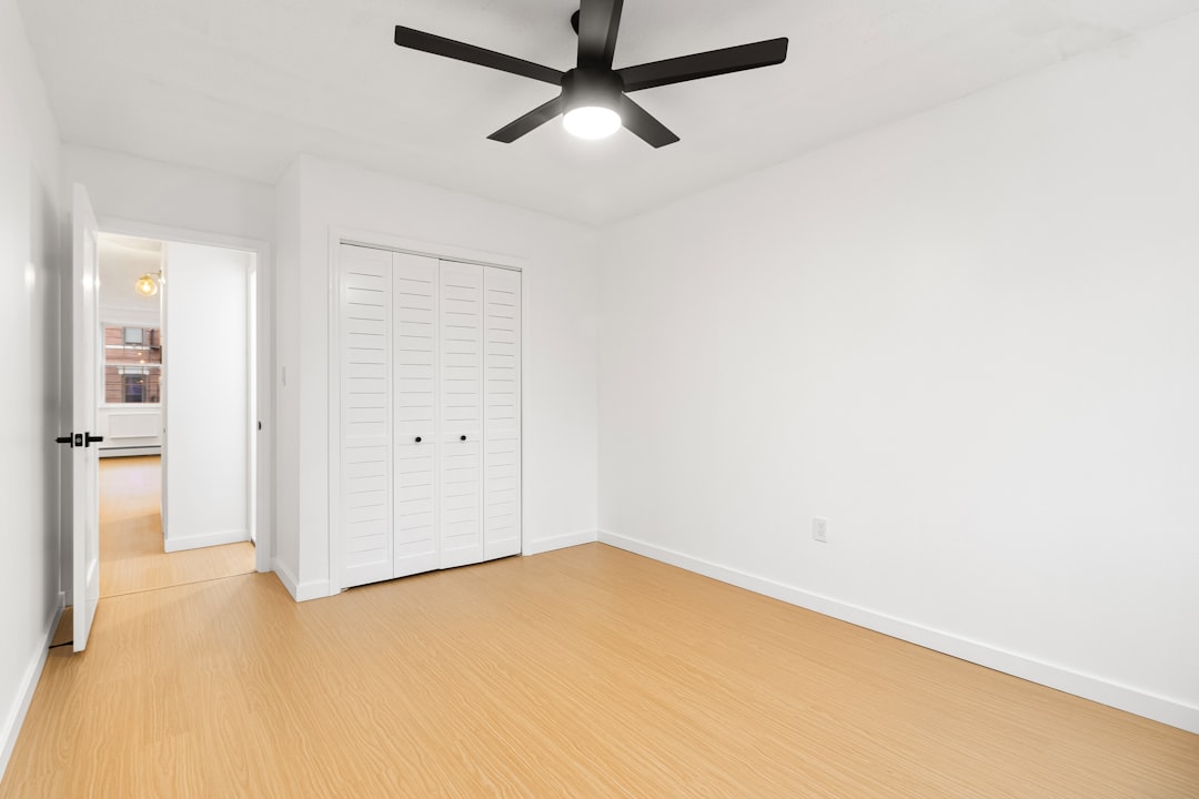 an-empty-room-with-a-ceiling-fan-and-white-walls-bi3oluk12by